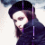 A person with long brown hair wearing a black beret and dark coat, shown in with subtle head movements against a light background