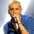 Static pixelated image of a person with light hair holding a microphone against a blue background.