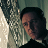 Pixelated static image of a person with dark hair in profile view against a blurred background with light and dark tones.