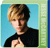 Pixelated image of a person with light brown hair wearing a black top against a blue background with green and blue border elements.
