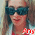 A person with long light brown hair wearing dark sunglasses and a light blue jacket over a red shirt, with red text reading "Any" at the bottom right.