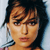 Pixelated close-up of a person with dark hair and light skin, wearing a light-colored earring, against a light blue background.