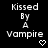 Black background with white pixelated text reading 'Kissed By A Vampire' and a small heart symbol below the word 'vampire'.