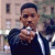 Static pixelated image of a person in dark clothing holding an object near their face against a blurred background with vertical elements.
