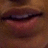A pixelated close-up of a person's mouth with lips slightly parted, showing teeth and part of the lower face against a brown background.