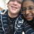 Two people in dark blue striped hooded jackets smile closely together against a light background.