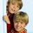 Three distinct poses of two young boys with light brown hair, wearing red and patterned shirts against blue backgrounds.
