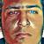 Pixelated close-up of a face with reddish-brown hair, blue eyes, and light skin tone against a multicolored background.