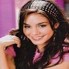 A person with long dark hair wearing a pink top and a headband with small white dots, smiling with hand near face against purple background.