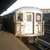 A subway train at a station with a bright light fixture above, viewed from a low angle on the platform.
