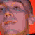 Pixelated close-up of a person's face with pinkish skin tones, dark hair, and orange-red background elements, rendered in low-resolution digital style.