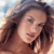 A pixelated close-up of a person with long brown hair, light skin, and a neutral expression against a blurred background.