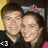 Two people with dark hair and pink bows stand side-by-side; one wears a black shirt, the other a pink top. The left person's mouth is open in a smile while the right person's mouth is closed.