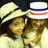Two figures in light-colored clothing with dark hair, one wearing a white hat with blue and red stripes, against a dark background.