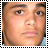 Pixelated close-up of a person's face with light brown skin, dark eyebrows, and visible eyes, nose, and mouth within a black-and-white striped border.