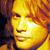Pixelated close-up of a person's face with warm yellow-orange tones, showing eyes, nose, mouth, and hair against a dark background.