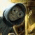 Pixelated static image of a character with dark hair and neutral expression leaning against a golden structure.