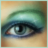 A close-up of a human eye with green and blue eyeshadow, featuring a visible eyeliner and a light-colored iris.