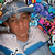 A person wearing a light blue cap and white-and-blue jacket with colorful pixelated background elements.