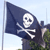 A pixelated dark blue flag with a white skull and crossbones symbol, mounted on a pole against a light blue sky background.