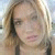 Pixelated close-up of a person with light brown hair holding a dark object near their face against a blurred background.