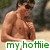 Pixelated image of a shirtless man with dark hair and sunglasses, standing on a beach with greenery in the background.