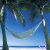 A static image of a beach scene with palm trees, hammock, and blue sky background.
