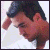 Pixelated close-up of a person with dark hair and reddish skin tone wearing a white shirt, head tilted downward.
