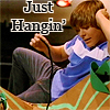 A person in a blue and white shirt and gray pants sits on a patterned couch with text reading 'Just Hangin'' above them.