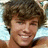 Pixelated close-up of a person with curly brown hair, light skin tone, and closed eyes smiling against a blurred background.