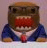 Pixelated static icon of a cartoon character with brown head, red mouth area, blue jacket, and white collar against light background.