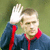 A pixelated figure in a dark blue jacket with red accents raises a white-gloved hand near their head against a blurred green background.