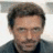 Pixelated static image of a person with short dark hair, light skin tone, and visible facial features including eyes, nose, mouth, and beard stubble.