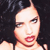 Pixelated close-up of a person with dark hair, light skin, and red lips, set against a dark background.