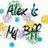 Pixelated static image with abstract shapes in green, blue, yellow, and purple tones on white background.
