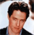 A pixelated close-up of a person with dark hair wearing a dark jacket over a light shirt against a light background.