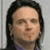 Pixelated portrait of a person with long dark hair, light skin, and a neutral expression against a light gray background.
