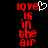 Red pixelated text 'love is in the air' with a white heart symbol replacing the 'o' in 'love' on the left side, against a black background.