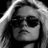 Black-and-white image of a person with long hair wearing dark sunglasses, displayed in a with four