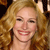 Pixelated close-up of a smiling person with long curly blonde hair, visible teeth, and light skin tone against a dark background.
