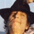 Pixelated close-up of a person wearing a black wide-brimmed hat with light-colored hair visible beneath, set against a pale blue background.