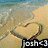 A beach scene with two heart-shaped sand drawings on the shore, one of which has a black banner with white text at the bottom.