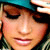 A pixelated close-up of a person wearing a teal cap, with visible eyes, nose, mouth, and dark hair against a blurred background.