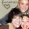 Three people pose closely together with smiles; a heart symbol and partial text appear in the background.