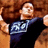 Pixelated image of a person with light brown hair wearing a dark shirt featuring a blue and white graphic design, set against a warm-toned background.