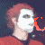 Pixelated figure with red hair and white mask-like face, wearing red shirt against dark background; orange text overlays in motion.