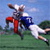 Pixelated static image of two football players in mid-action on a grassy field with blue sky background, one player wearing red pants and white helmet, the other in dark jersey and white uniform.