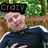 A pixelated image of a person in a dark blue shirt with white stripes on the sleeves, positioned against a green foliage background with a wooden fence.