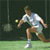 Pixelated static image of a tennis player in mid-action on a green court with dark background, wearing white shirt and shorts, holding racket, yellow ball visible.