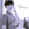 A grayscale image of a person with short dark hair wearing a light-colored shirt, standing with arms crossed against a bright background with text reading 'Zac efron' in the upper right.